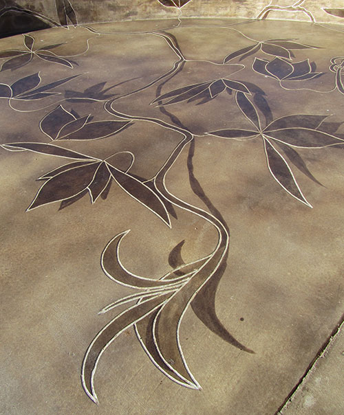 Floral vines applied with acid stain on a concrete slab. Using the same color of acid stain in varying strength gives the perception of depth.