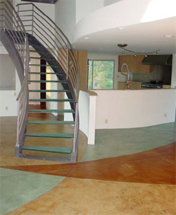 This living room space equipped with open stairs to the second floor shows a concrete floor thath as been stained in three colors, green, tan and brown