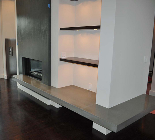 A modern concrete fireplace with the hearth continuing throughout the space under the bookcase and around the corner.