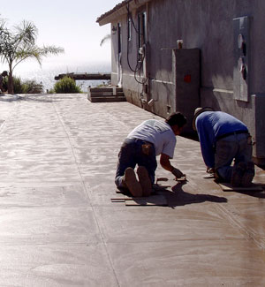 Two contractors using a saw-cut joint tool on a large concrete patio